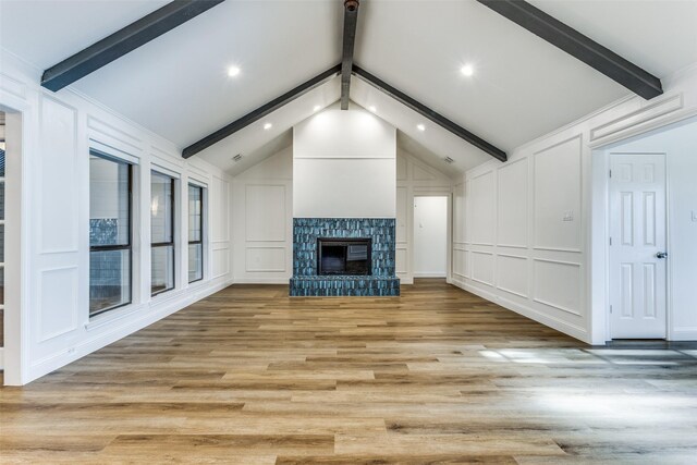 unfurnished living room with vaulted ceiling with beams, light hardwood / wood-style floors, and a stone fireplace