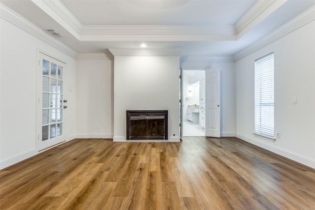 unfurnished living room featuring light wood-type flooring, a raised ceiling, and ornamental molding