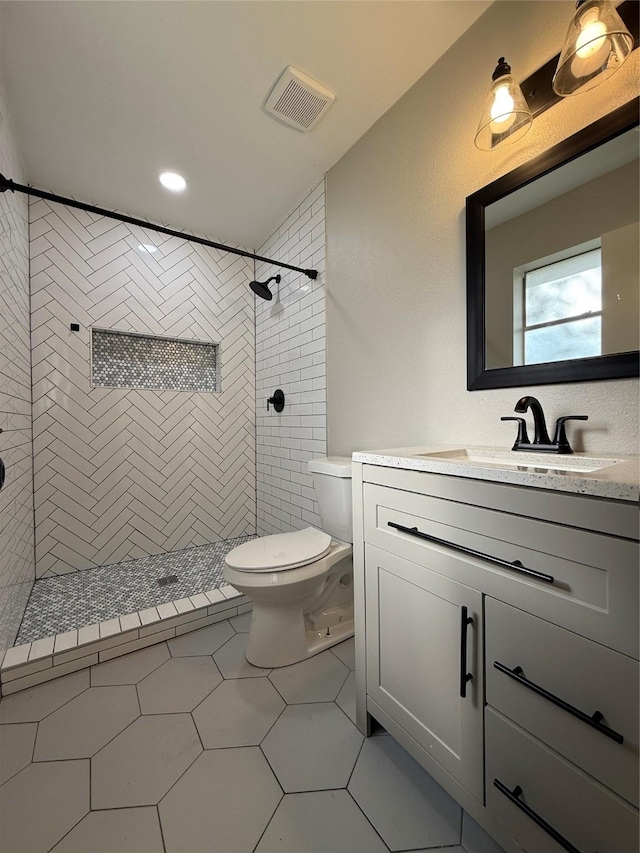 bathroom featuring a tile shower, tile patterned flooring, vanity, and toilet