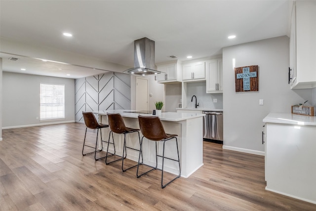 kitchen with dishwasher, white cabinets, a breakfast bar area, light hardwood / wood-style flooring, and island exhaust hood