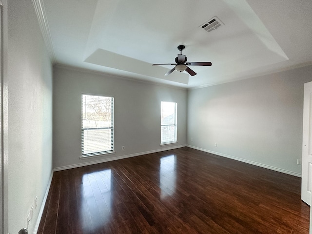 empty room with a ceiling fan, ornamental molding, visible vents, a raised ceiling, and dark wood-style floors