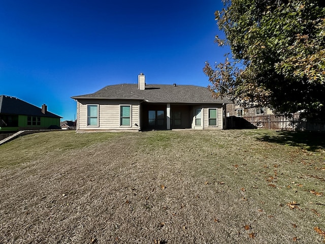 back of property with fence, a shingled roof, a lawn, and a chimney