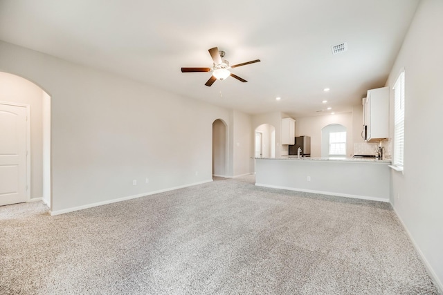 unfurnished living room with sink, light colored carpet, and ceiling fan