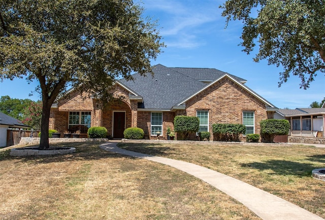 view of front of property featuring a front lawn, a shingled roof, and brick siding