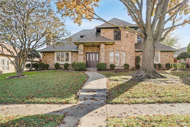 view of front facade with a shingled roof, a front yard, and brick siding