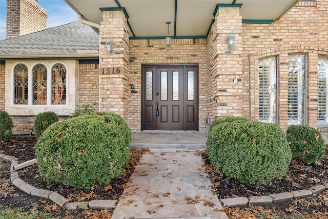 doorway to property with roof with shingles, brick siding, and a chimney