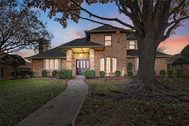 traditional-style house with a shingled roof, french doors, a chimney, a yard, and brick siding