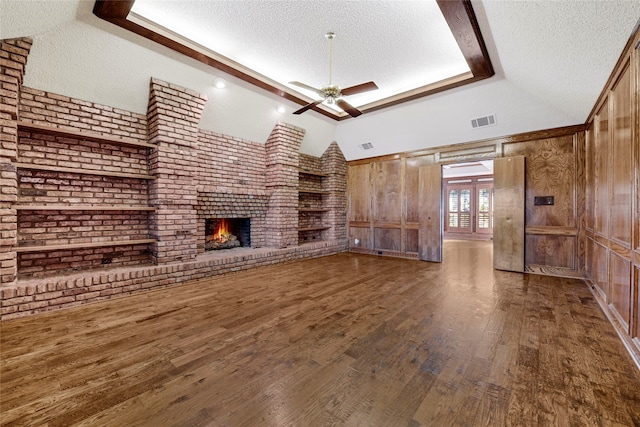 unfurnished living room with a textured ceiling, dark hardwood / wood-style floors, a raised ceiling, ceiling fan, and a fireplace