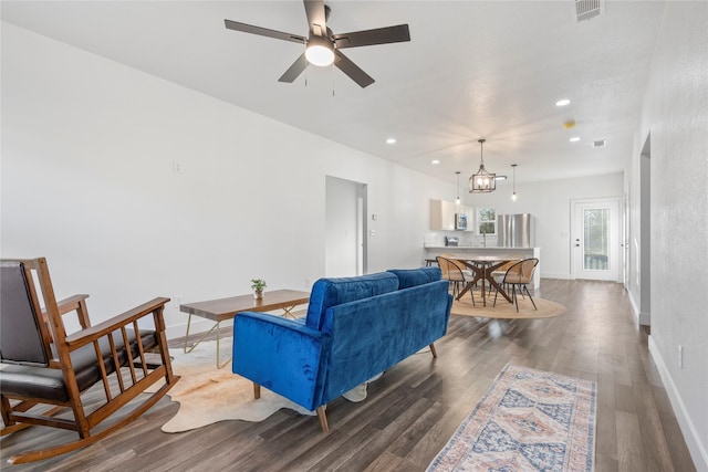 living room featuring ceiling fan with notable chandelier and dark wood-type flooring