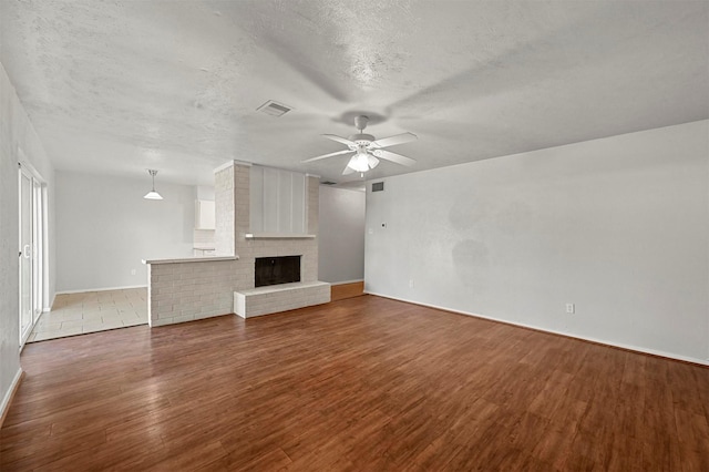 unfurnished living room with a textured ceiling, ceiling fan, dark hardwood / wood-style floors, and a brick fireplace