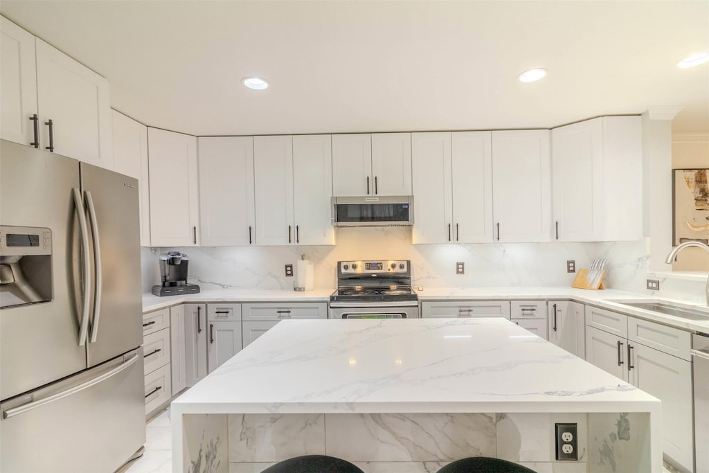 kitchen featuring stainless steel appliances, sink, white cabinetry, light stone counters, and a breakfast bar