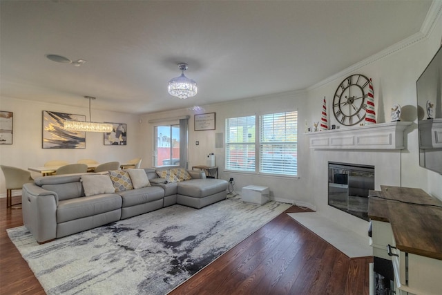 living room with a tile fireplace, crown molding, a notable chandelier, and dark hardwood / wood-style flooring