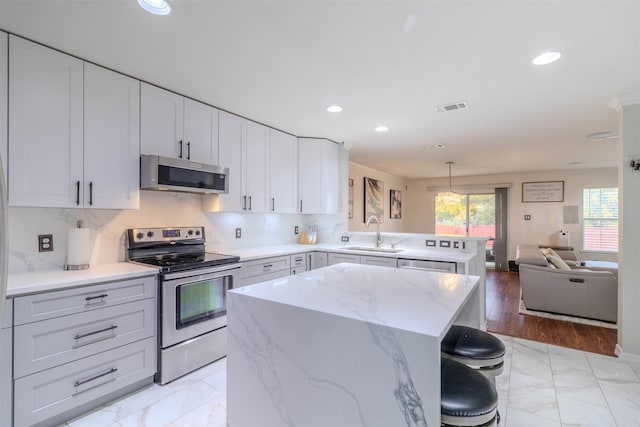 kitchen with stainless steel appliances, sink, a center island, a breakfast bar area, and hanging light fixtures