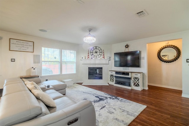 living room with a notable chandelier, crown molding, a fireplace, and dark hardwood / wood-style flooring