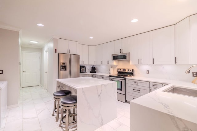 kitchen with a breakfast bar, light stone counters, a kitchen island, stainless steel appliances, and white cabinets