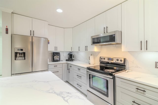 kitchen with tasteful backsplash, stainless steel appliances, light stone counters, and white cabinets