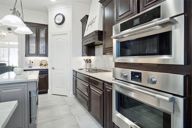 kitchen featuring crown molding, decorative light fixtures, dark brown cabinets, appliances with stainless steel finishes, and backsplash