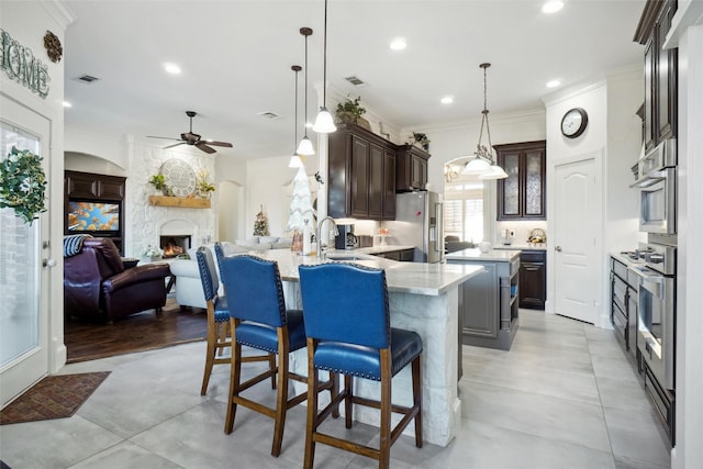 kitchen featuring appliances with stainless steel finishes, decorative light fixtures, ornamental molding, dark brown cabinetry, and kitchen peninsula