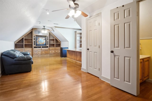 interior space featuring built in shelves, light wood-type flooring, a textured ceiling, and vaulted ceiling