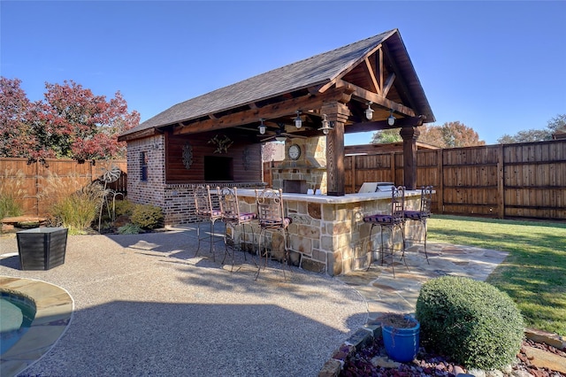 view of patio featuring a bar, ceiling fan, a gazebo, and an outdoor stone fireplace