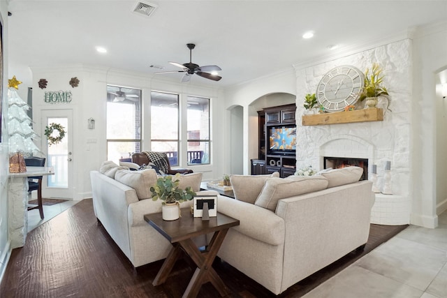 living room with a stone fireplace, plenty of natural light, ornamental molding, and hardwood / wood-style flooring