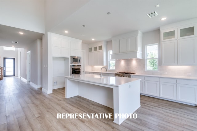 kitchen with a center island with sink, light hardwood / wood-style floors, white cabinetry, and appliances with stainless steel finishes