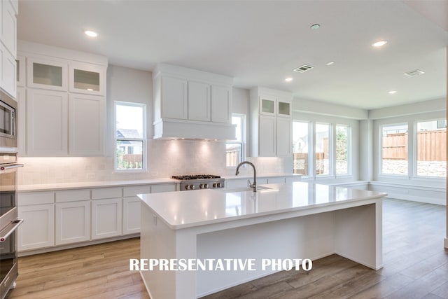 kitchen featuring white cabinetry, sink, an island with sink, and light wood-type flooring