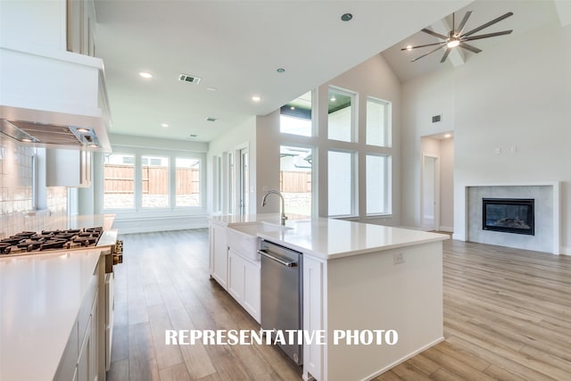 kitchen featuring a tile fireplace, sink, an island with sink, white cabinets, and light wood-type flooring