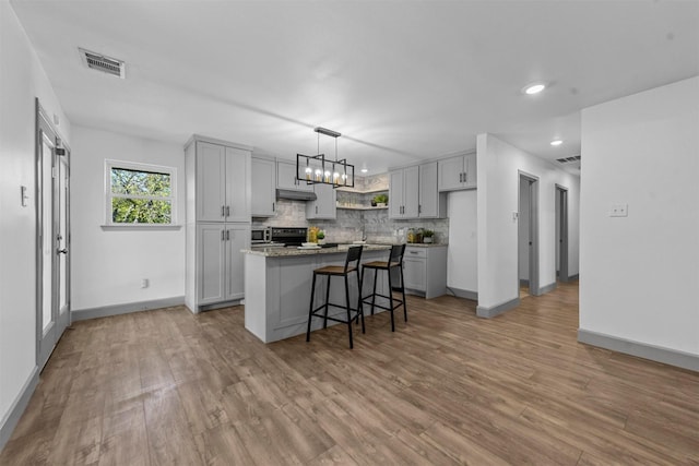 kitchen with light wood-type flooring, a kitchen bar, a center island, and gray cabinets