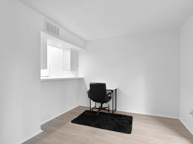 home office with a textured ceiling and light hardwood / wood-style floors