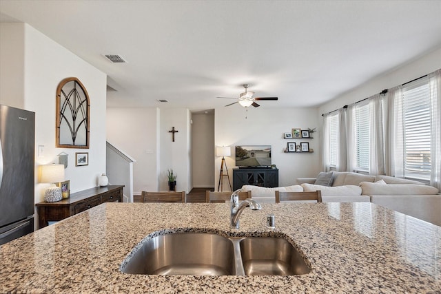 kitchen with refrigerator, sink, ceiling fan, and stone countertops