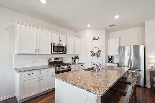 kitchen with light stone countertops, appliances with stainless steel finishes, a kitchen island with sink, sink, and white cabinets