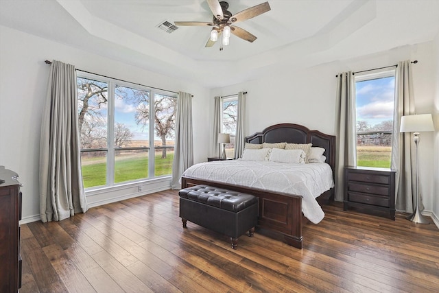 bedroom featuring a tray ceiling, visible vents, dark wood-type flooring, a ceiling fan, and baseboards