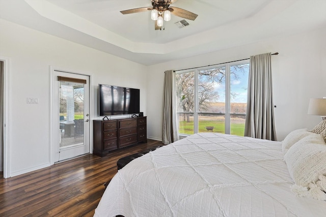 bedroom featuring wood finished floors, visible vents, baseboards, access to exterior, and a tray ceiling