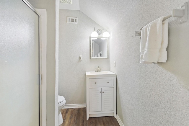 bathroom with a textured wall, toilet, wood finished floors, vanity, and visible vents