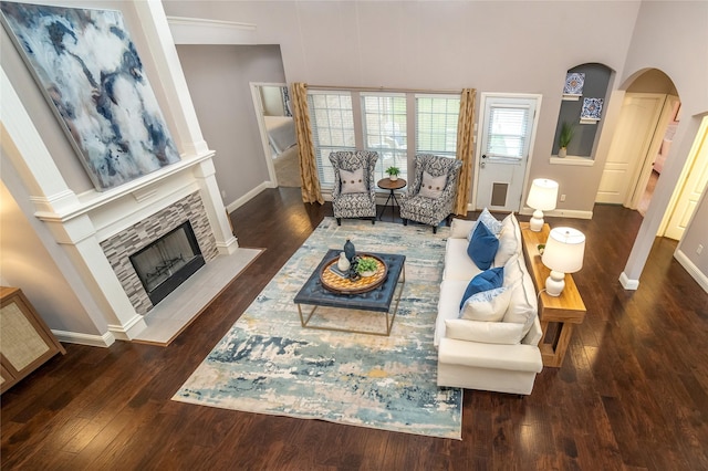 living room featuring a high ceiling, a stone fireplace, and dark wood-type flooring