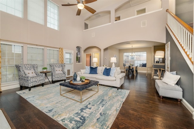 living room featuring ceiling fan with notable chandelier, dark hardwood / wood-style flooring, and a towering ceiling