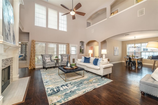 living room featuring ceiling fan with notable chandelier, a high ceiling, dark hardwood / wood-style flooring, and a stone fireplace