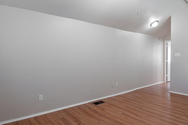 unfurnished room with a textured ceiling, wood-type flooring, and lofted ceiling