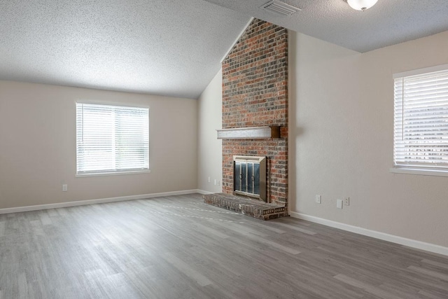 unfurnished living room with hardwood / wood-style floors, lofted ceiling, a textured ceiling, and a brick fireplace