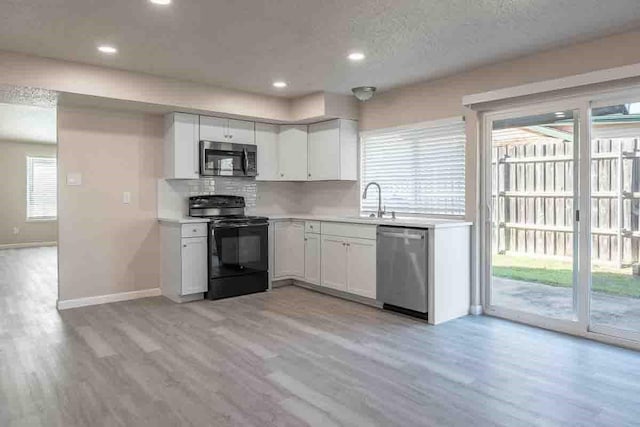 kitchen with light wood-type flooring, stainless steel appliances, white cabinetry, and backsplash