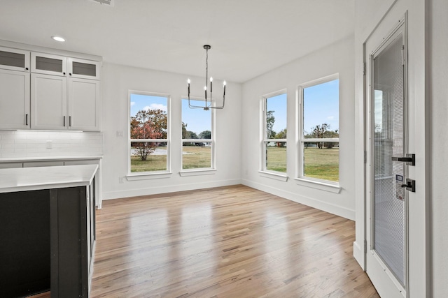 unfurnished dining area with a healthy amount of sunlight, light hardwood / wood-style floors, and an inviting chandelier