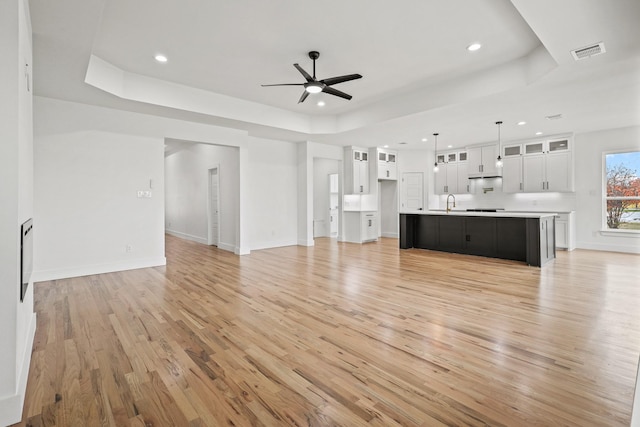 unfurnished living room with light wood-type flooring, a tray ceiling, and ceiling fan