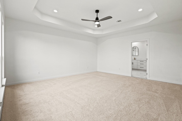 unfurnished bedroom with carpet, ceiling fan, connected bathroom, and a tray ceiling