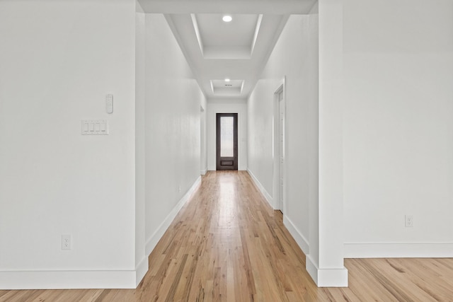 corridor with a raised ceiling and light hardwood / wood-style flooring