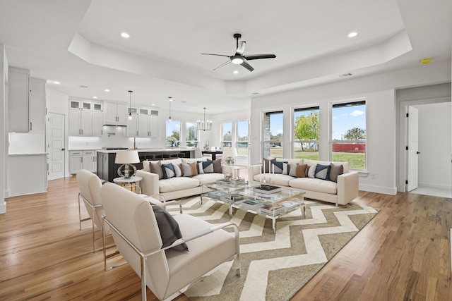 living room with ceiling fan with notable chandelier, light hardwood / wood-style floors, and a raised ceiling