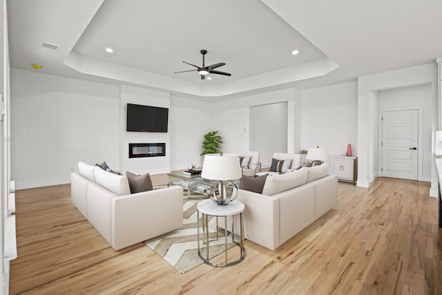 living room with a raised ceiling, light hardwood / wood-style flooring, and ceiling fan