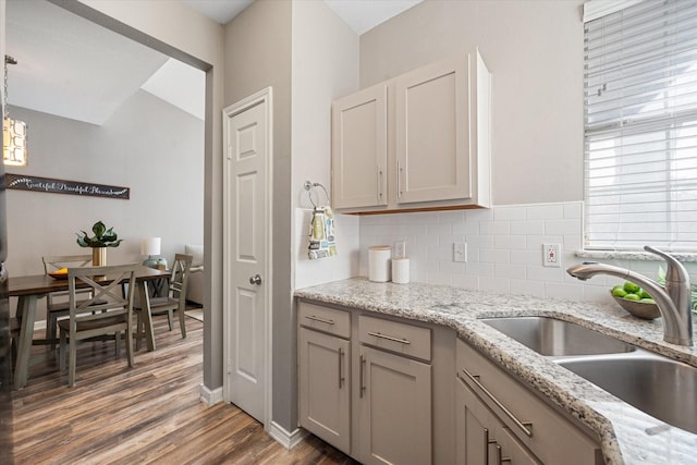 kitchen with sink, backsplash, hanging light fixtures, light stone countertops, and dark wood-type flooring