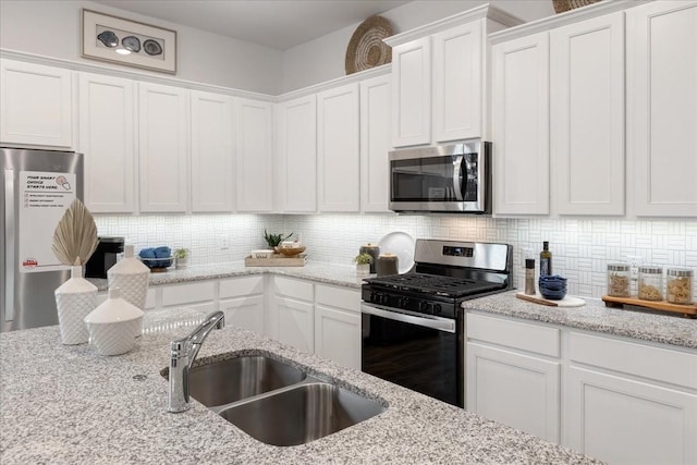 kitchen with light stone countertops, white cabinetry, sink, stainless steel appliances, and decorative backsplash