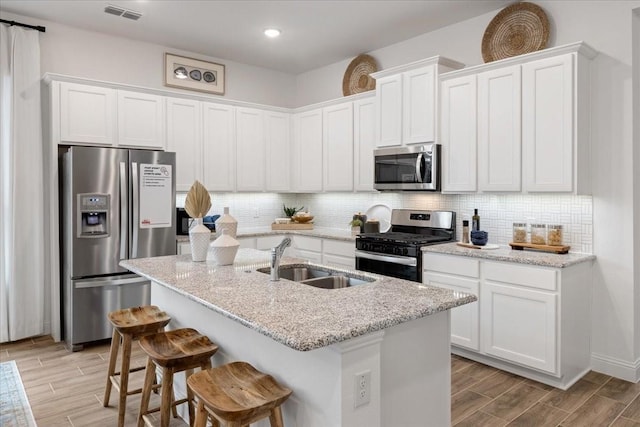 kitchen with white cabinetry, sink, light stone counters, a center island with sink, and appliances with stainless steel finishes